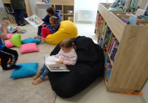 Dzieci na dużych pufach oglądają książki.